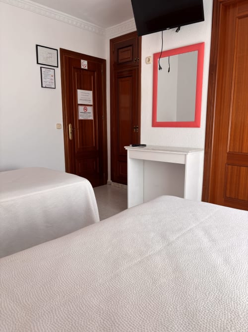 Habitación doble de Hostal Las Dunas con dos camas, escritorio blanco, espejo marco rojo, TV y puertas de madera en Cabo de Gata