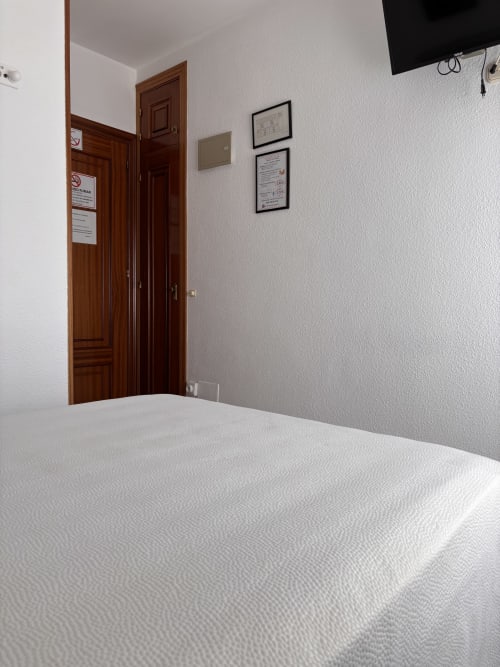 Habitación Individual Superior del Hostal Las Dunas en Cabo de Gata con cama blanca, puerta de madera, TV mural y cuadro enmarcado