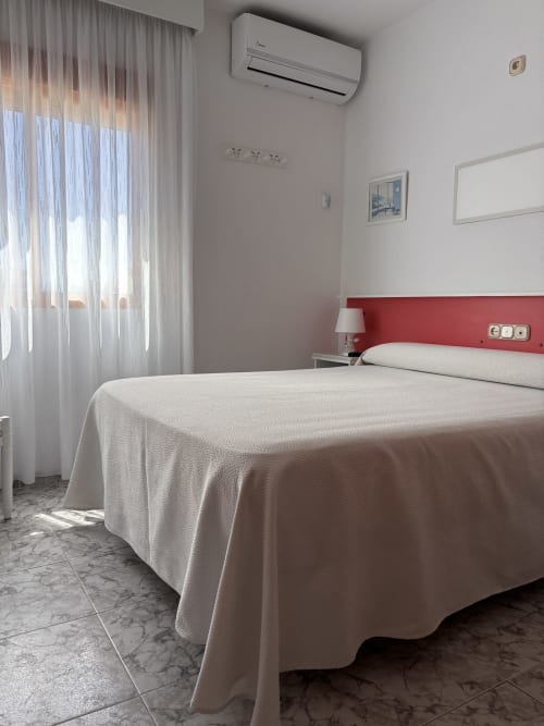 Habitación Single Superior en Hostal Las Dunas, Cabo de Gata: cama con cabecero rojo, aire acondicionado y ventana luminosa