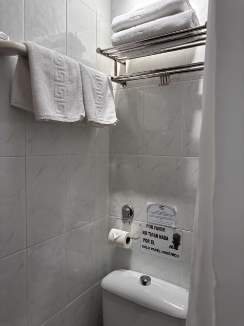 Baño de Hostal Las Dunas con toallero cromado, azulejos blancos y cartel de higiene en español en Cabo de Gata
