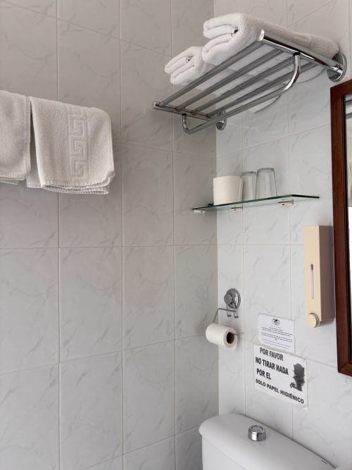Estante del baño con toallas blancas enrolladas, artículos de tocador y cartel de higiene en Hostal Las Dunas, Cabo de Gata