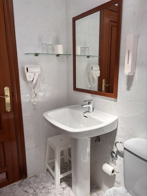 Baño moderno del Hostal Las Dunas con lavamanos pedestal, espejo, secador de pelo mural y dispensador de jabón en Cabo de Gata