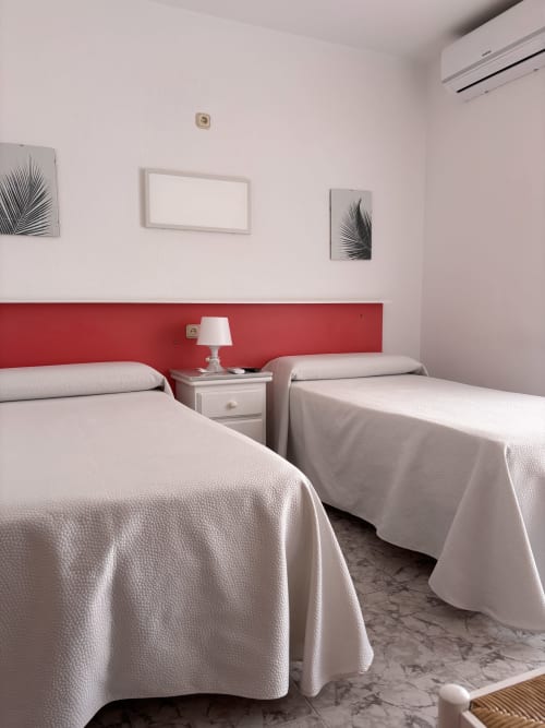 Camas gemelas en habitación moderna del Hostal Las Dunas, Cabo de Gata con pared acentuada en rojo y aire acondicionado