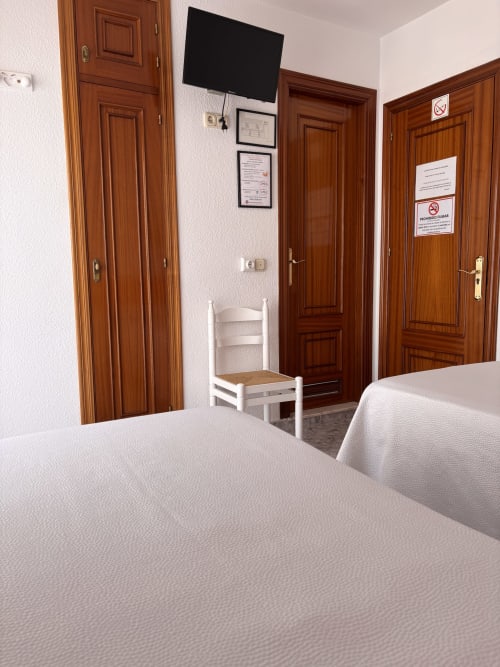 Habitación Superior individual en Hostal Las Dunas, Cabo de Gata, con puertas de madera, ropa de cama blanca, televisor y decoración sencilla