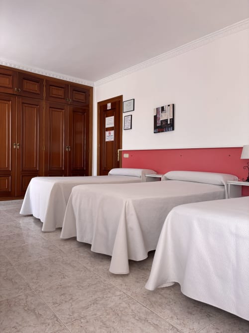 Habitación triple con terraza en Hostal Las Dunas, Cabo de Gata Almería, con tres camas de sábanas blancas y rojo