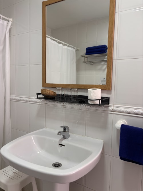Baño limpio con espejo en Hostal Las Dunas, Cabo de Gata, con azulejos blancos y toallas azules