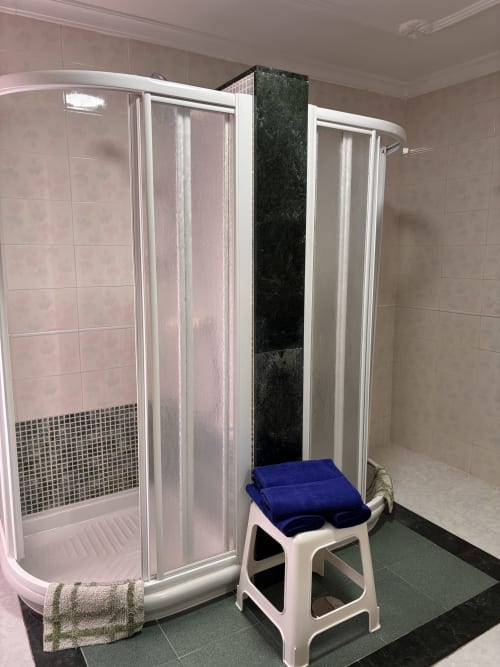 Baño moderno con ducha de cristal curvado en Hostal Las Dunas de Cabo de Gata, con azulejos rosados y escalón blanco