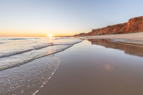 Nascer do sol na Praia do Algarve com falésias douradas, águas calmas e reflexo tranquilo na costa de Portugal