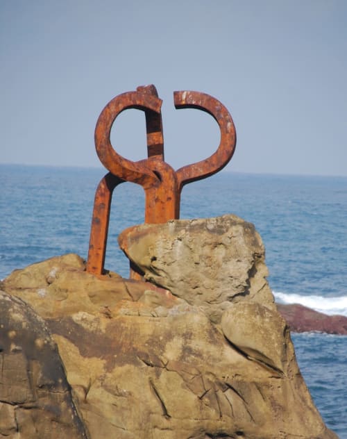Escultura de hierro oxidado en rocas costeras con vistas a la bahía de San Sebastián