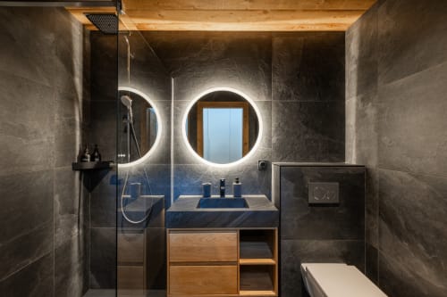 Modern bathroom in Altitudia villa Chalet Magy 3 Les Gets with dual illuminated mirrors, wooden vanity and dark tile accents