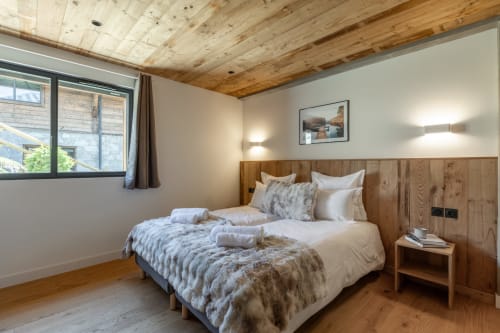 Cozy bedroom in Chalet Magy 3 with wooden beams, twin beds, mountain view window, and rustic wood paneling at Altitudia, Les
