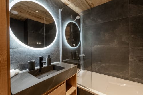 Modern bathroom in Chalet Magy 3 at Altitudia with LED-lit circular mirror, marble vanity, and glass shower enclosure