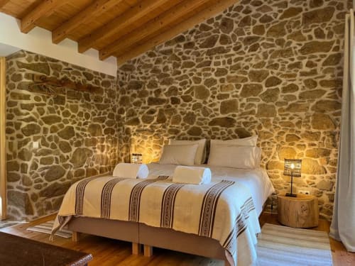 Quarto rústico de pedra em Quinta da Mata de Baixo com teto de vigas aparentes, cama queen e iluminação acolhedora em Cagida, Portugal
