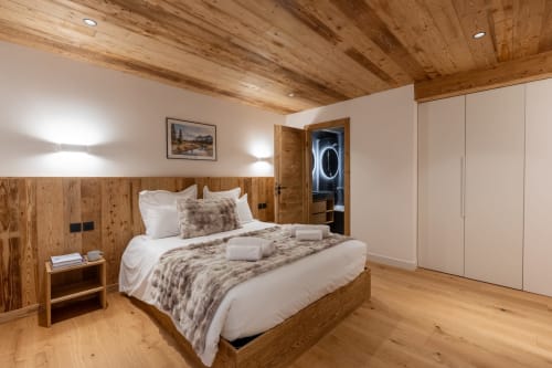 Luxurious chalet bedroom at Altitudia with wooden ceiling, queen bed, white cabinetry, and modern ensuite in Scionzier