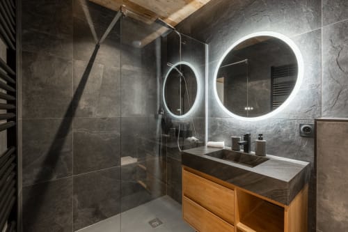 Modern luxury bathroom in Altitudia chalet with dark tile, LED mirrors, wooden vanity, and walk-in shower