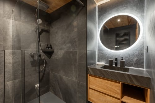 Modern bathroom in Altitudia Chalet Magy 3 with illuminated mirror, rainfall shower, wooden vanity, and slate tile walls