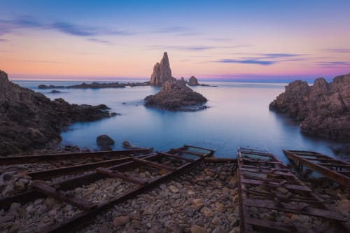 Dramatic sunset over rocky coves and sea stacks at Cabo de Gata, with weathered wooden boats on the shore near Hostal Las