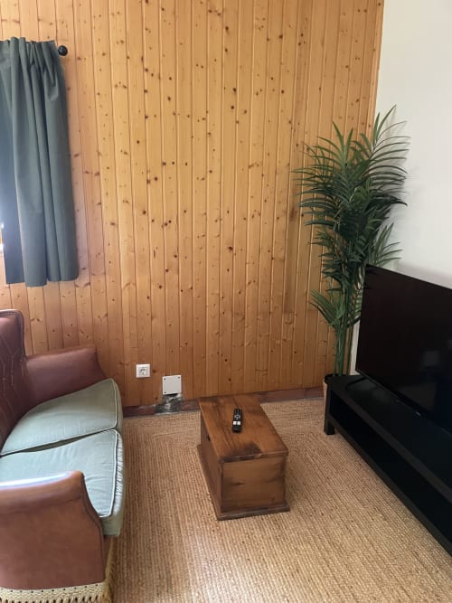 Sala de estar del apartamento Monte Roblo con pared de madera, sofá de cuero marrón, mesa de madera, televisor de pantalla plana, planta en maceta y
