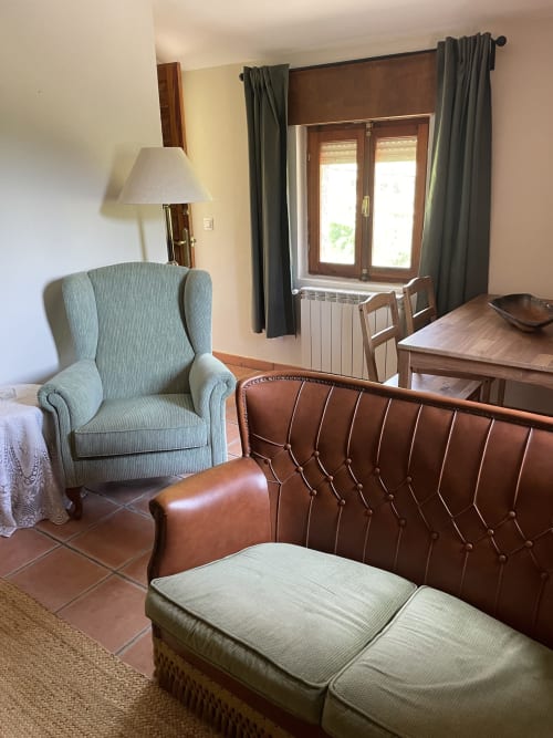 Sala de estar del apartamento Monte Roblo con sofá de cuero, sillón orejero y vistas a la montaña a través de puertas de madera
