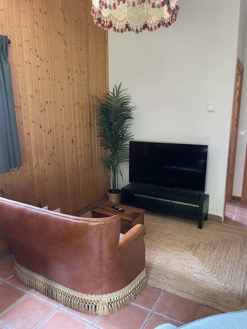 Sala de estar del apartamento Monte Roblo con sillón de cuero marrón, televisor de pantalla plana, planta en maceta y paneles de madera en la pared