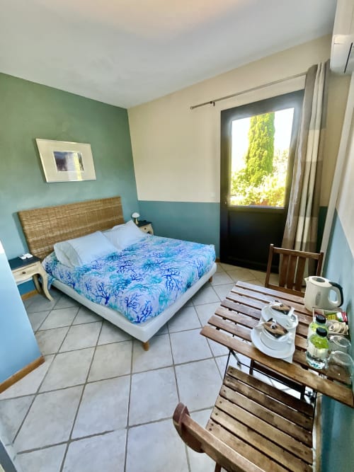 Chambre lumineuse au Domaine Pero Longo à Sartène avec murs turquoise, lit en rotin et vue montagne par porte vitrée