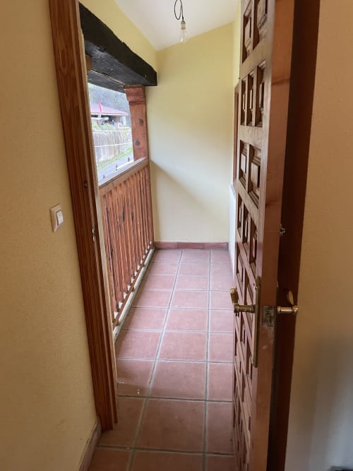 Estrecho pasillo con piso de baldosas terracota, paredes amarillas, puertas de madera y vistas a través de ventana en apartamento Monte Roblo, Salamon