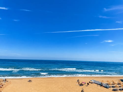 Słoneczny widok na plażę Torremolinos ze złotym piaskiem, falami z białymi grzbietami i czystym niebieskim niebem z tarasu apartamentu