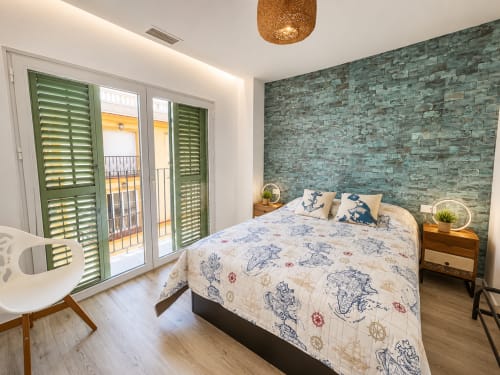 Nowoczesna sypialnia w apartamencie w Torremolinos z pościelą nautyczną, zieloną ścianą akcentową z kamienia, drewnianymi szafkami nocnymi i balkonem