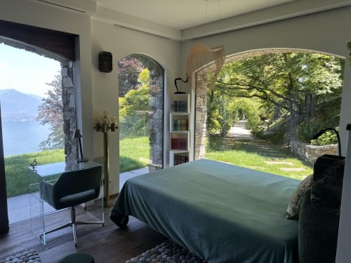 Luxurious bedroom with bed, black chair, and open doors to panoramic lake and garden views at Italian spa retreat