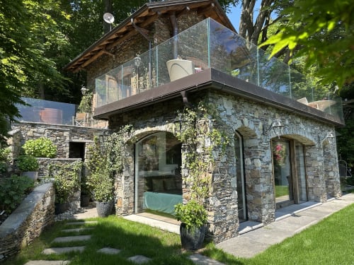 Luxury stone cottage with glass-enclosed terrace overlooking Lake Maggiore, surrounded by lush greenery in Stresa, Italy