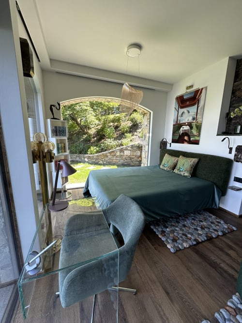 Deluxe studio bedroom with green bedding, desk chair, lake view terrace overlooking Lake Maggiore, wood flooring, and garden