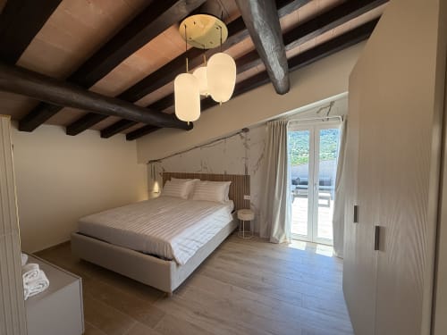 Suite moderna a Borgo Albador Rooms a Torpè con travi a vista, lampadari sospesi e vista sulle montagne attraverso le vetrate