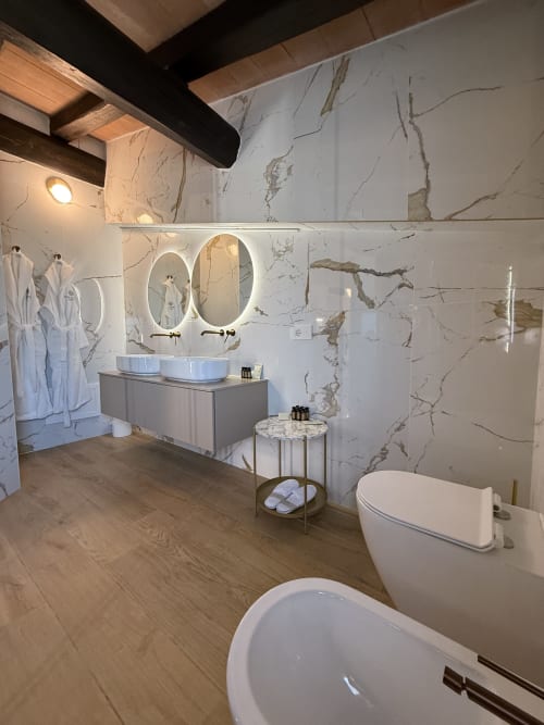 Bagno moderno della Borgata Albador Suite a Torpè con pareti in marmo, doppi lavabi, specchi illuminati e finiture bianche