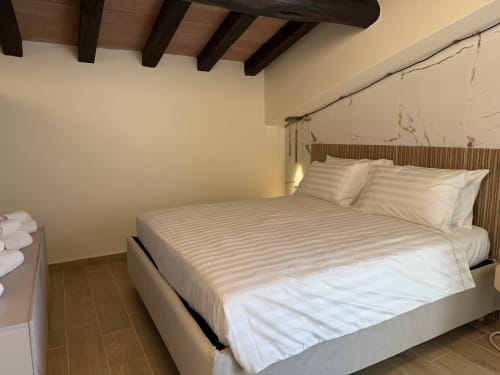 Suite moderna a Borgo Albador Rooms a Torpè con letto queen, travi in legno a vista e parete in marmo
