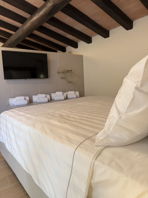 Suite moderna a Borgo Albador con biancheria color crema, TV a schermo piatto, travi a vista e arredamento minimalista a Torpè, Italia
