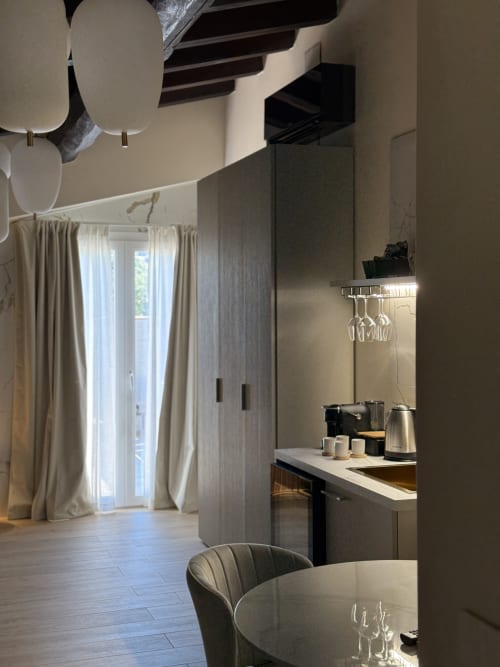 Suite moderna a Borgo Albador Rooms a Torpè con angolo cottura, zona pranzo e vista montagna attraverso porte-finestre con tende