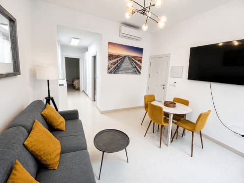 Nowoczesny salon w Torremolinos z szarą sofą, poduszkami w kolorze musztardy, stołem jadalnym, telewizorem LCD i współczesnym wystrojem