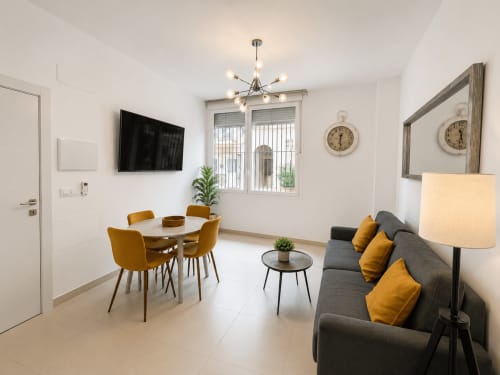 Nowoczesny salon w apartamencie w Torremolinos z szarą sofą, stołem jadalnym, TV i akcentami musztardowymi