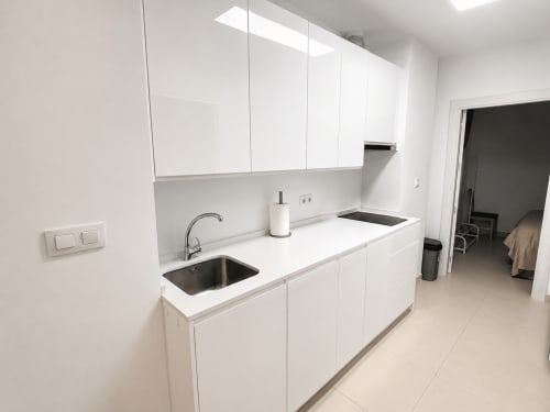 Nowoczesna biała kuchnia z zlewozmywakiem ze stali nierdzewnej, błyszczącymi szafkami i oknem dachowym w apartamencie w Torremolinos