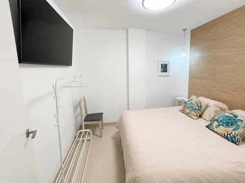 Nowoczesna sypialnia w apartamencie w Torremolinos z łóżkiem, drewnianą ścianą akcentową, telewizorem i poduszkami o morskiej tematyce