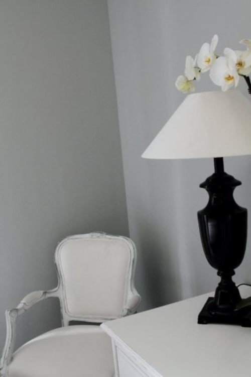 Elegante angolo della camera da letto al B&B Le Biciclette con poltrona bianca imbottita, lampada da tavolo nera, paralume bianco e orchidee bianche