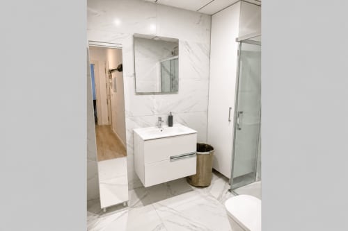 Nowoczesna łazienka w apartamencie w Torremolinos z białą umywalką, marmurowymi płytkami, lustrem i szklana kabiną prysznicową
