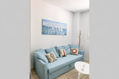 Jasnoniebieski rozkładany fotel w nowoczesnym apartamencie w Torremolinos z sztuką przedstawiającą panoramę miasta, białym stolikiem kawowym i elementami drewnianymi