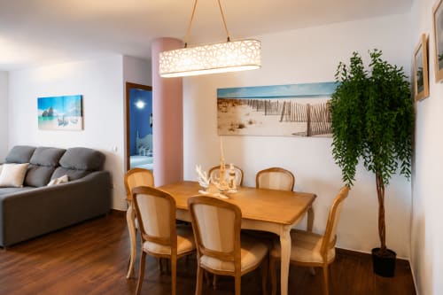 Nowoczesna jadalnia w apartamencie Zahara de los Atunes ze stołem drewnianym, krzesłami, lampa wisząca i salonem z szarą sofą