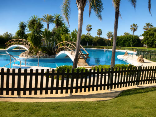 Tropikalny ogród z zakrzywionymi drewnianymi mostkami nad jasnonieskim prywatnym basenem w Alquileres Cantos de Sirena, Torremolinos