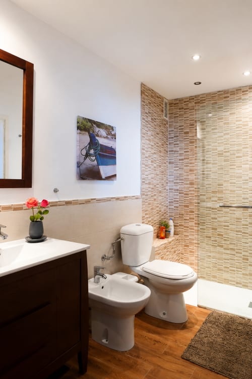 Nowoczesna łazienka w apartamencie w Zahara de los Atunes z wyłożoną kafelkami prysznicem, toaletą, bidetem, drewnianą umywalką i kwiatami dekoracyjnymi