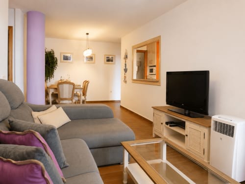 Jasny, nowoczesny salon z szarą sofą, telewizorem ekranowym i meblami drewnianymi w apartamencie Cantos de Sirena Torremolinos