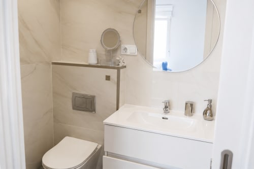 Nowoczesna łazienka z prysznicem, białą szafką z umywalką i okrągłym lustrem w apartamencie do wynajęcia w Torremolinos