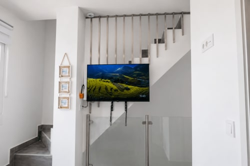 Nowoczesny interior apartamentu w Torremolinos z telewizorem na ścianie wyświetlającym górski krajobraz, schody z metalowymi poręczami