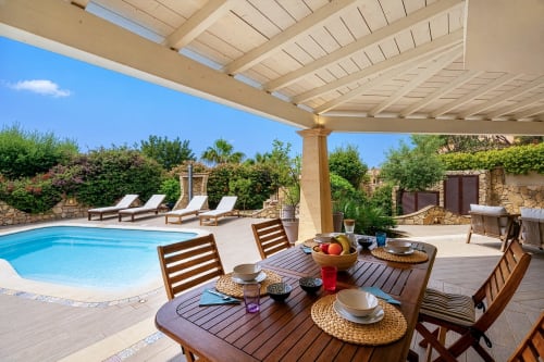 Luxury villa patio with dining table, swimming pool, loungers, and pergola in Quartu Sant'Elena, Sardinia